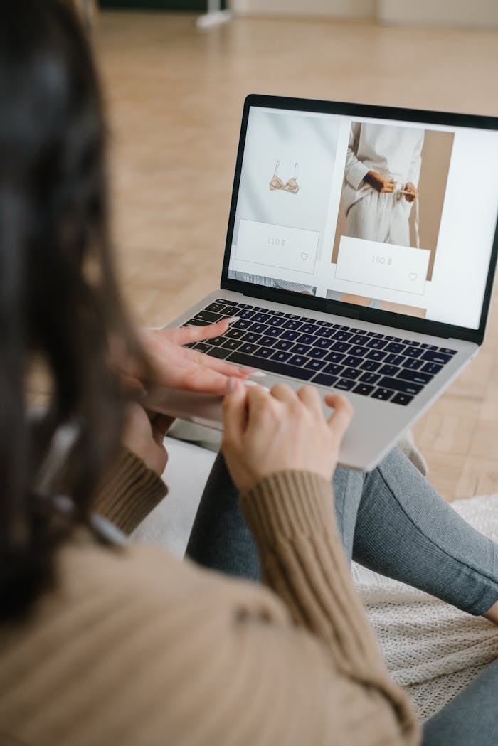 Female browsing an online fashion store on a laptop indoors, focusing on clothing and accessories.