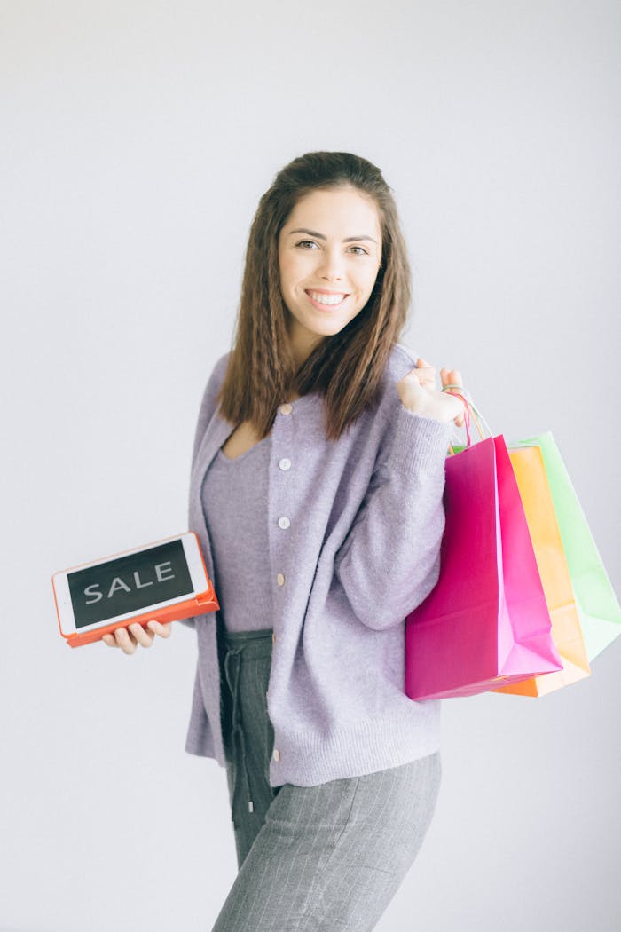 Smiling woman holding colorful shopping bags and a tablet with a sale notification.