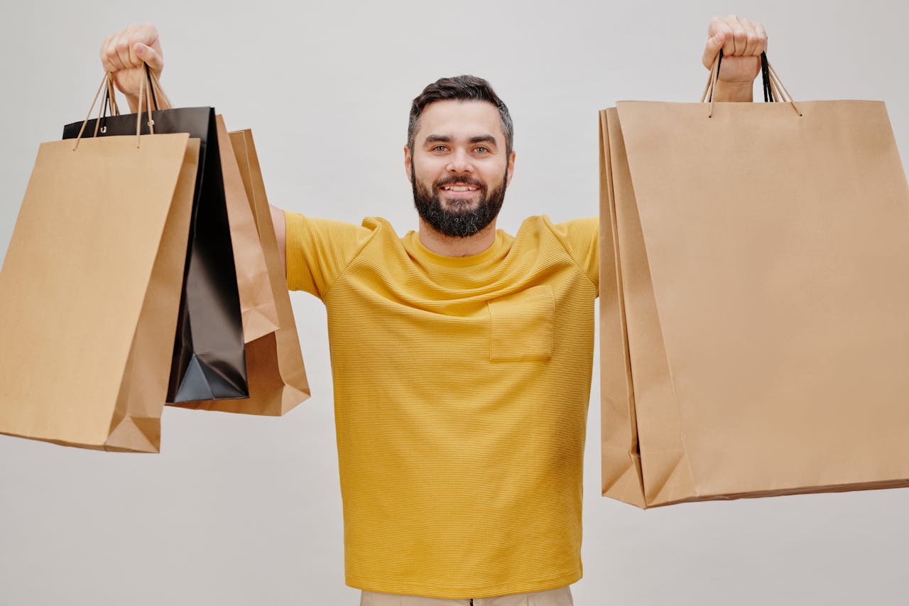 Happy man in yellow shirt holding multiple shopping bags, expressing joy of shopping.